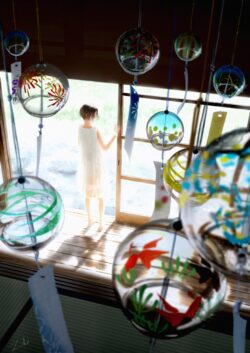 Girl in bright doorway Japanese wind chimes (Fūrin) summer atmosphere sunlight interior scene traditional Japanese room goldfish motif art clear glass orbs blur foreground background serene moment shining light