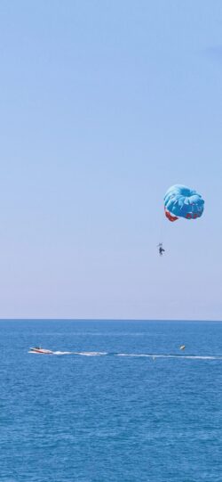 parasailing over sea blue ocean speed boat clear sky water sports summer activity aerial view vacation adventure marine recreation distant boat bright day horizon line parachute coastal leisure bl