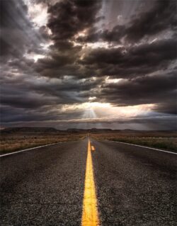 open road highway storm clouds dramatic sky sun rays crepuscular rays desert landscape travel journey adventure freedom asphalt horizon cloudy