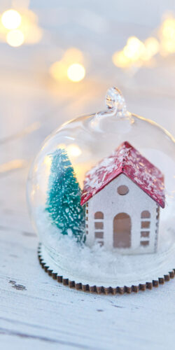snow globe winter house christmas tree miniature holiday decor festive season warm lights cozy home aesthetic white wood background xmas