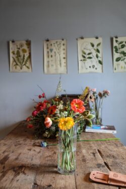 floral arrangement poppies interior decor vintage style botanical posters rustic table flower vase home studio artistic living natural light floral design creative workspace aesthetic room decor