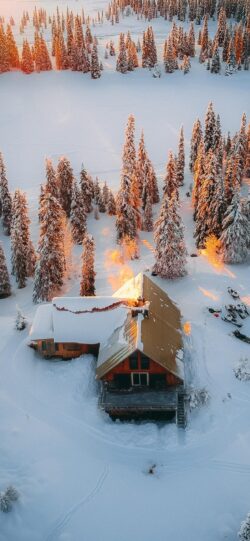 snowy cabin aerial view winter forest pine trees golden light sunset glow remote lodge wilderness retreat ski resort winter landscape log cabin snow covered roof cold climate nature background mou
