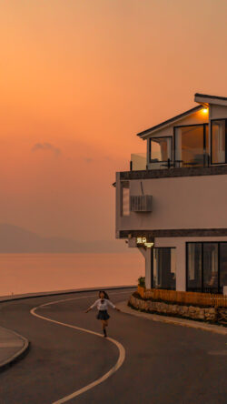 sunset road lakeside resort girl running orange sky golden hour modern architecture coastal road romantic setting vacation property evening light curved road peaceful lake traveler travel destinati