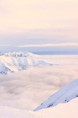 snowy mountains thick fog winter clouds alpine landscape pastel colors mountain peaks cold weather high altitude above the clouds peaceful scene white mountains blue and pink sky winter wonderland